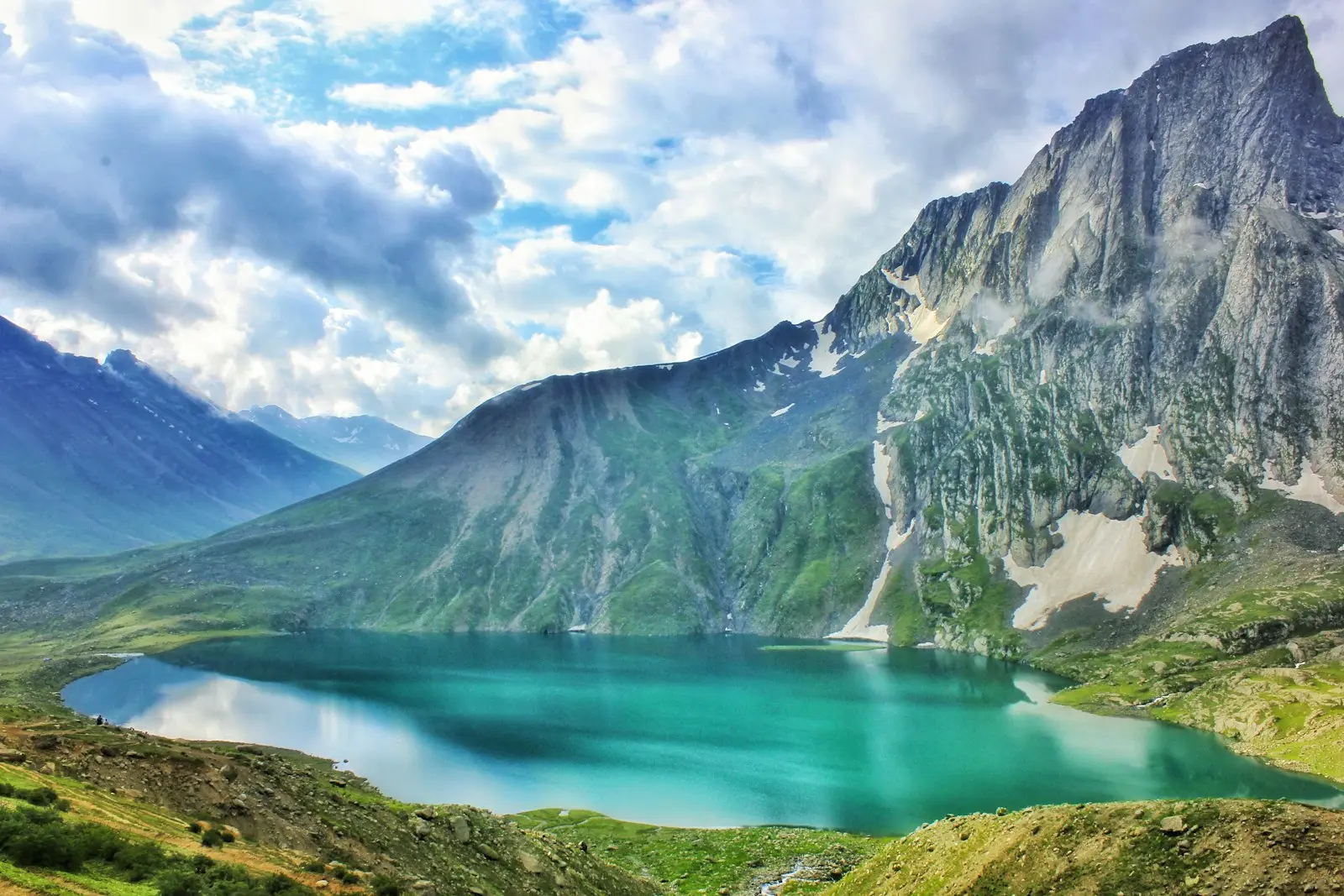 Turquoise lake below steep mountains under a cloudy sky