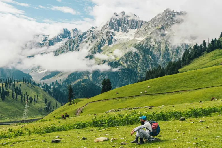 Hiker resting on a green mountain slope under the clouds